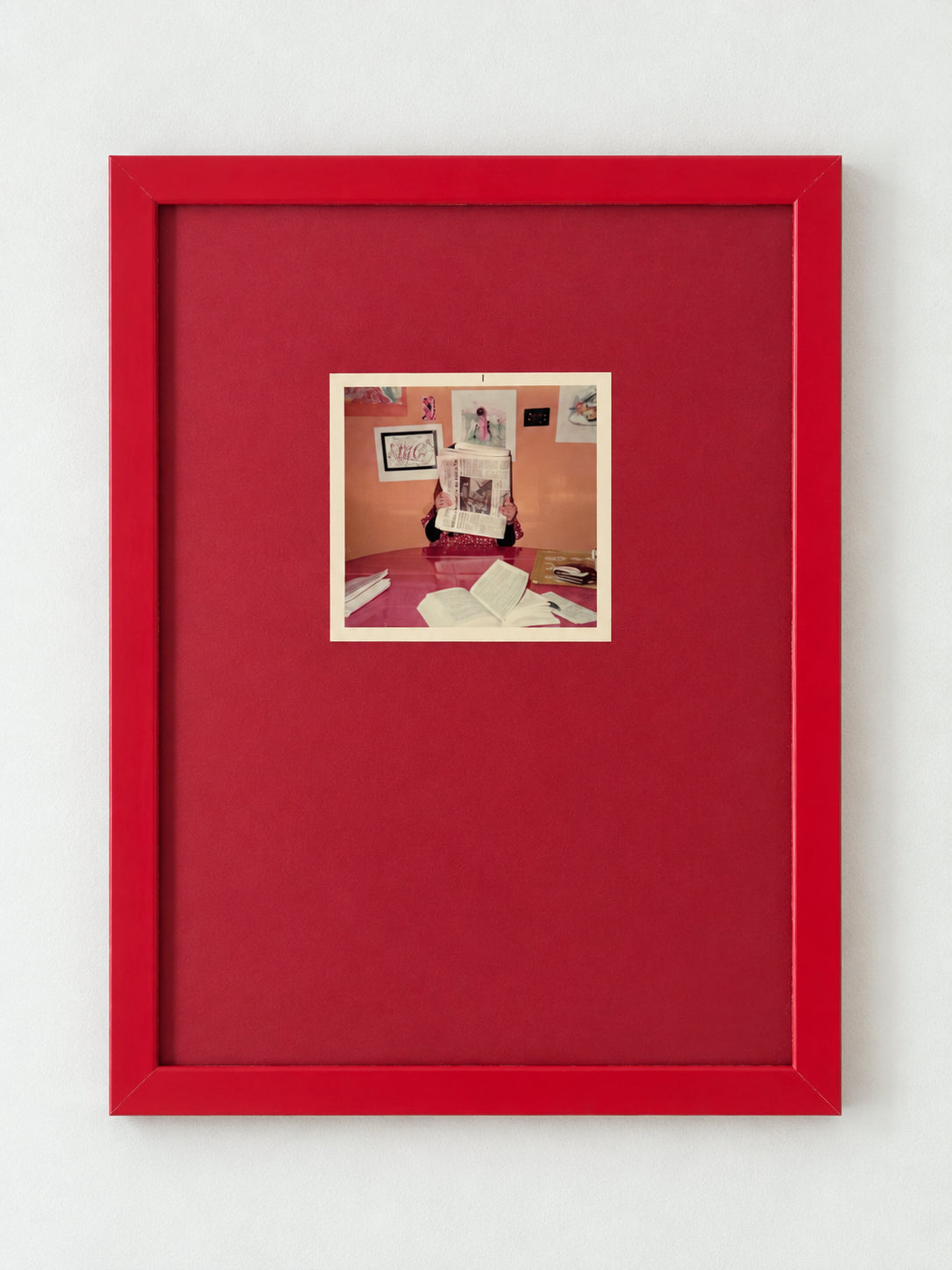 Vintage photograph of a figure reading a newspaper, float mounted on a red mat in a red frame