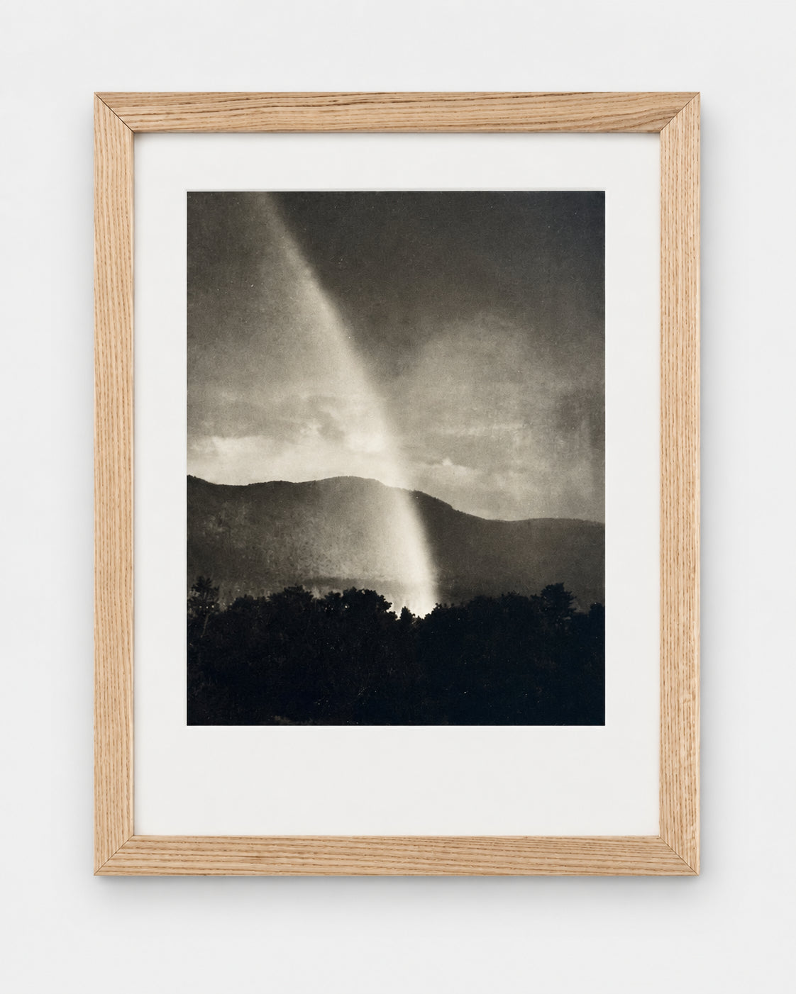 Vintage photograph of a funnel cloud over dark hills, matted in a light oak frame