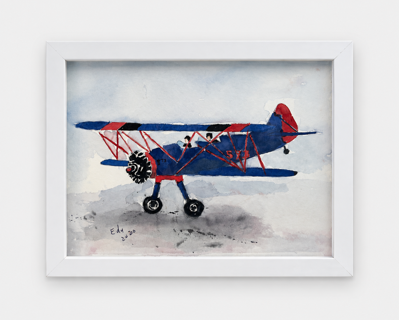 Watercolor painting of a red and blue vintage biplane, signed and dated 2000, in a white wood frame