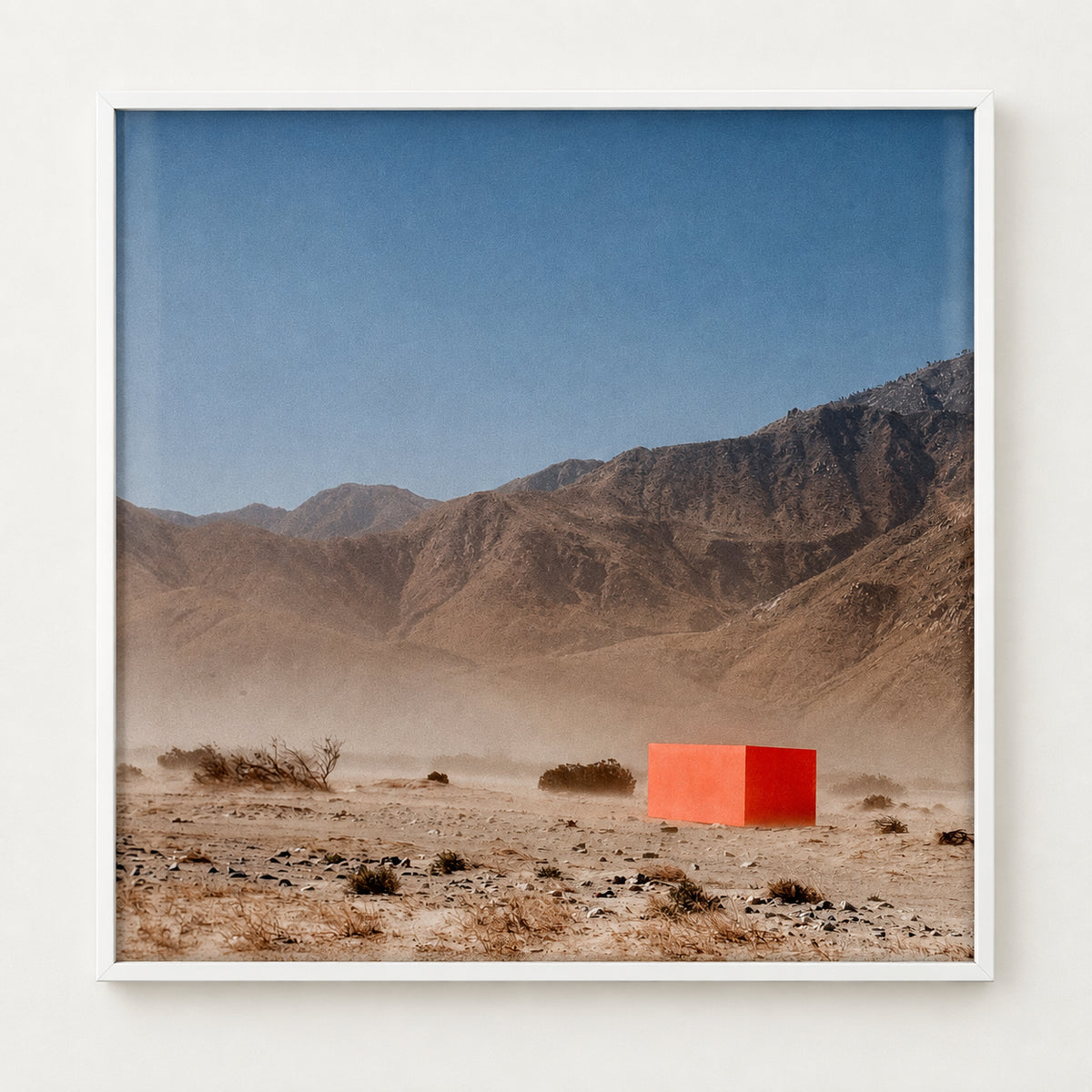 Photograph of a bright orange cube in a dusty desert landscape with mountains, in a white frame