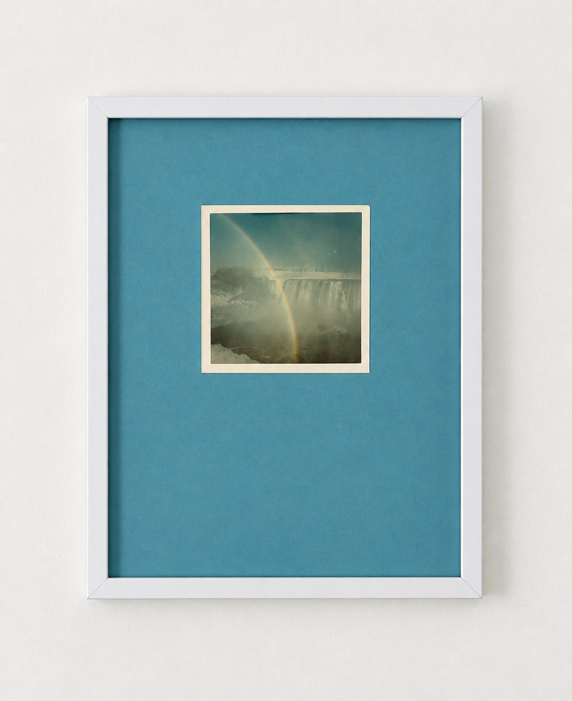 Vintage photograph of a rainbow over a waterfall, float mounted on a blue mat in a white frame